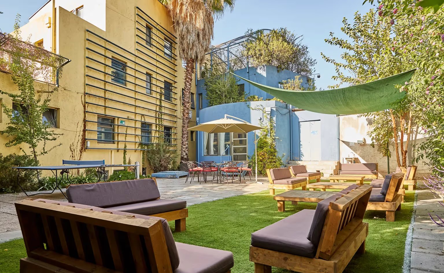 Jardín interior de Clínica Los Tiempos, con mobiliario de madera bajo una malla verde